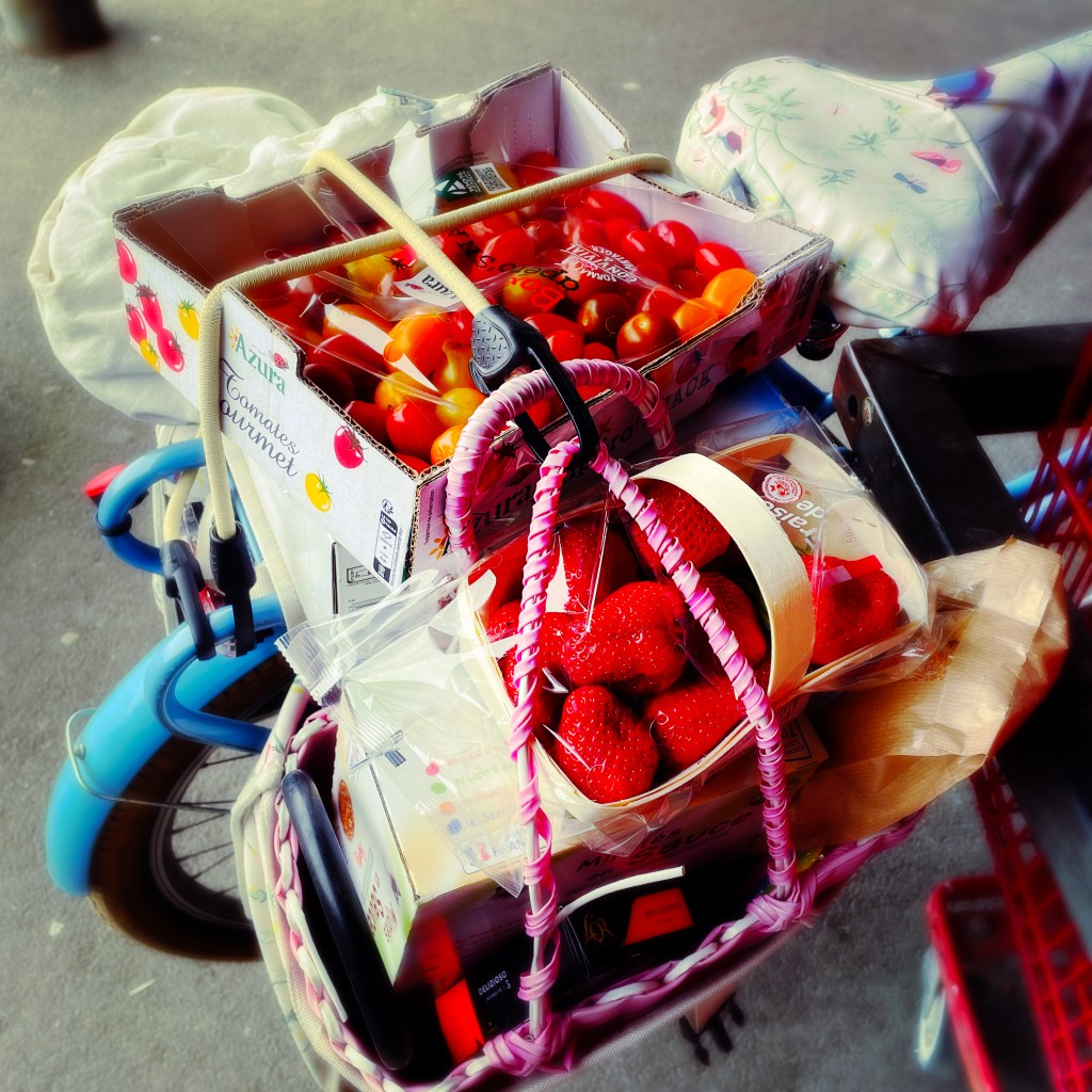 Vue d'une cagette de tomates sur le porte bagage et d'une barquette de fraises au sommet de la sacoche du vélo
