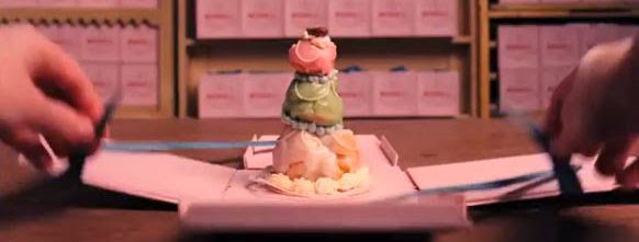 Gardien de prison ouvrant une boîte rose de la pâtisserie Mendel — The Grand Budapest Hôtel — Wes Anderson