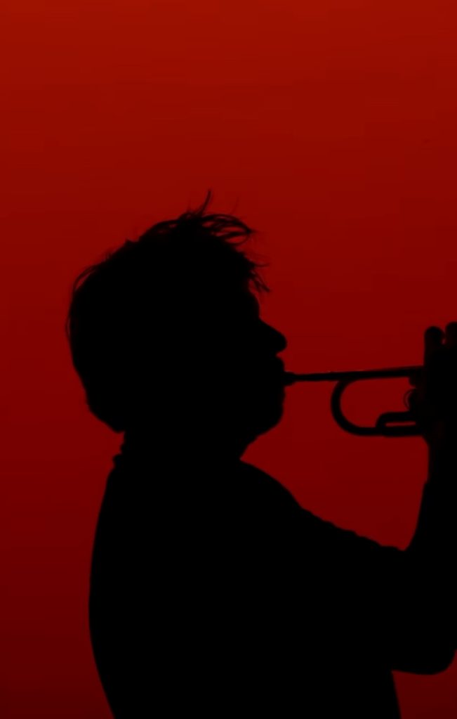 Screen shot de la vidéo short de Forever - un des membre de Ghinzu joue de la trompette en silhouette noire face à un écran rouge